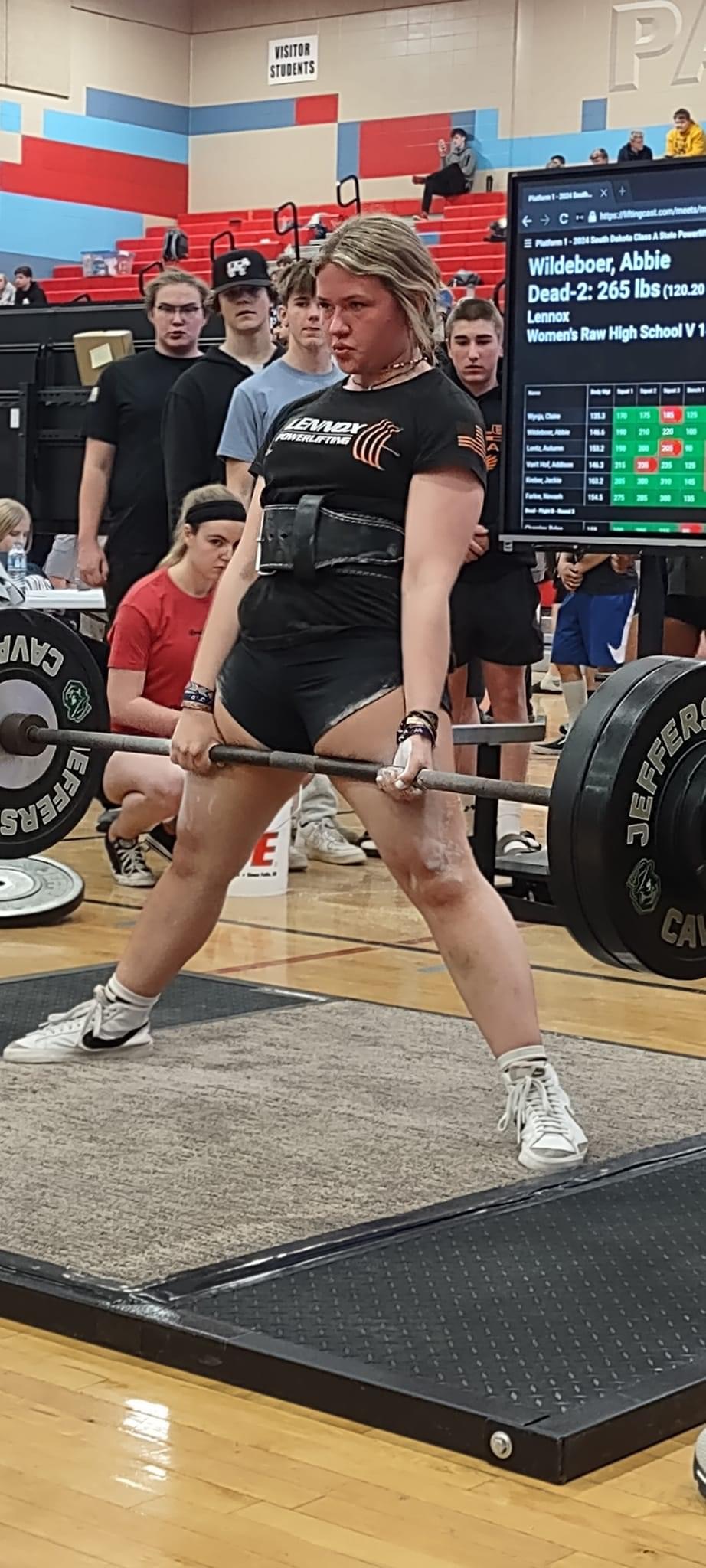 Powerlifter completing a deadlift with spectators behind the platform