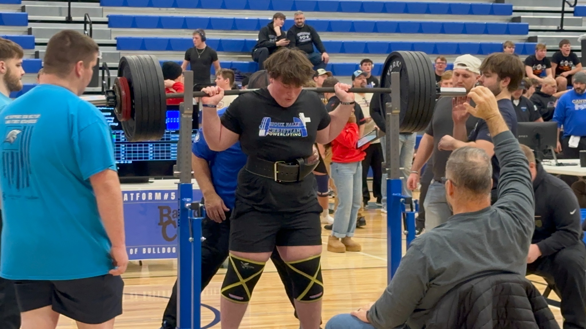 Powerlifter preparing to squat with spotters at a high school meet